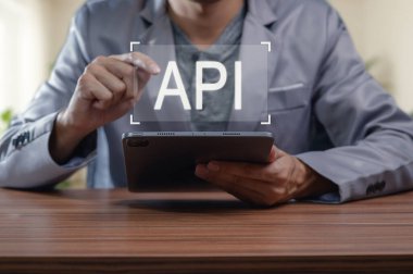 API terimini gösteren dijital tabletle odaklanmış bir birey, programlama ve modern teknoloji arasındaki bağlantıyı sembolize ediyor. Bu resim, profesyonel bir ortamda yenilik ve kullanıcı katılımını temsil eder..
