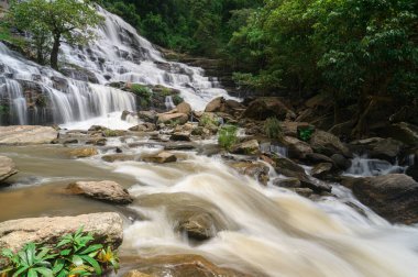 Chiang Mai, Tayland 'da çarpıcı bir şelalenin huzur veren güzelliğini keşfedin. Bu resim sahnesinde kayaların üzerinden akan sular yemyeşil ve davetkar doğayla çevrili..