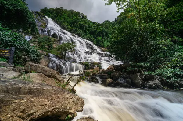 Chiang Mai 'deki şelalenin nefes kesici güzelliğini keşfedin, canlı yeşillik ve dramatik bulutlar tarafından çerçevelenmiş, doğa severler ve gezginler için mükemmel..