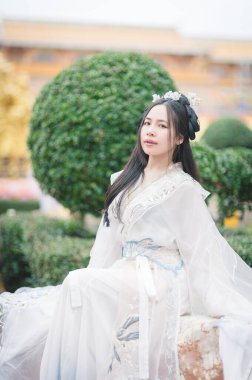 Zarif Hanfu kıyafetleri içinde genç bir kadın huzurlu bir bahçede zarif poz veriyor, geleneksel Çin kültürünün zerafetini güzel yeşillikler arasında somutlaştırıyor..