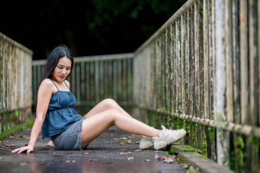 Bereketli bir ormanda, kırsal bir köprüde otururken huzurlu bir anın tadını çıkaran bir kadın. Güzel bir ortamda, doğayla olan huzuru ve bağlantıyı somutlaştırıyor..