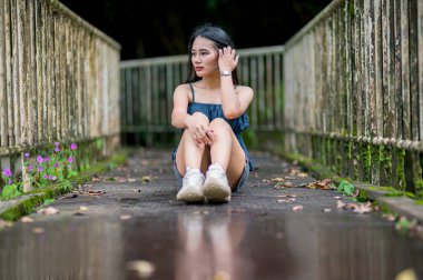 Doğanın ve huzurun özünü somutlaştıran, yemyeşil bir orman yolunda çiçeklerle çevrili, eski ahşap bir köprüde oturan bir kızın huzurlu bir anı..