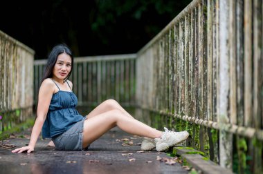 Genç bir kadın güzel bir orman ortamında kırsal bir köprüde huzurlu bir anın tadını çıkarıyor. Yeşillik ve doğal ışık, dinlenmek ve keşfetmek için ideal huzurlu bir atmosfer yaratır..