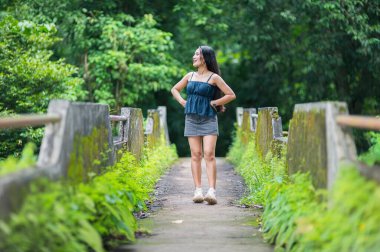 Genç bir kadın büyüleyici bir orman yolunda duruyor, doğanın güzelliğini kucaklıyor. Bereketli yeşil çevre macera ve gençleşme için ideal sakin bir atmosfer yaratıyor..