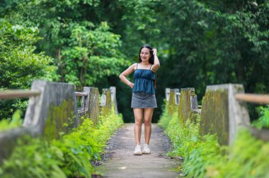 Genç bir kadın, yemyeşil yemyeşil ile çevrili, sakin bir orman yolunda güvenli bir şekilde poz verir, sakin bir açık hava ortamında doğayı keşfetmenin keyfini somutlaştırır..