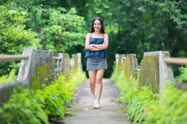 Genç bir kadın sakin bir orman yolunda güvenle geziniyor. Yeşillik ve canlı ağaçlarla çevrili sahne, doğadaki rahatlama ve neşeyi somutlaştırıyor..