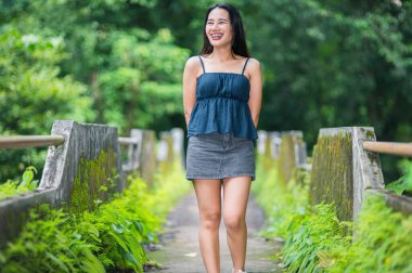 Neşeli bir kadın, yemyeşil ve canlı doğayla çevrili sakin bir orman yolunda yürüyor. Bu büyüleyici sahne, açık hava macerasının ve sükunetin özünü yansıtıyor..