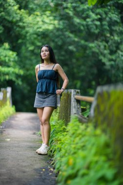 Genç bir kadın orman yolunda huzur içinde duruyor, canlı yeşilliği ve rahatlatıcı atmosferi içine çekiyor. Bu görüntü doğa keşiflerinin ve sükunetin özünü yakalar..