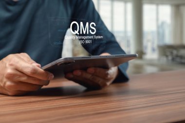 İş geliştirme için verimlilik ve ISO standartlarına odaklanan, Kalite Yönetim Sistemi arayüzü gösteren bir tablet kullanan bir kişinin yakın plan görüntüsü.