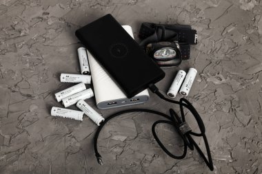  Siyah ve beyaz güç bankaları, farlar ve gri arka planda alkalin piller. Elektrik kesintisi ve elektriksiz yaşama hazırlıkları. Üst görünüm.