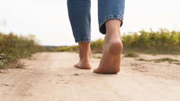 Woman walking in field meadow. Close-up of bare feet soiled with the ground. Female legs on a rural sand road. Healthy lifestyle concept.