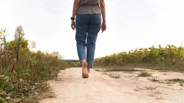 Woman walking in field meadow. Close-up of bare feet soiled with the ground. Female legs on a rural sand road. Healthy lifestyle concept.