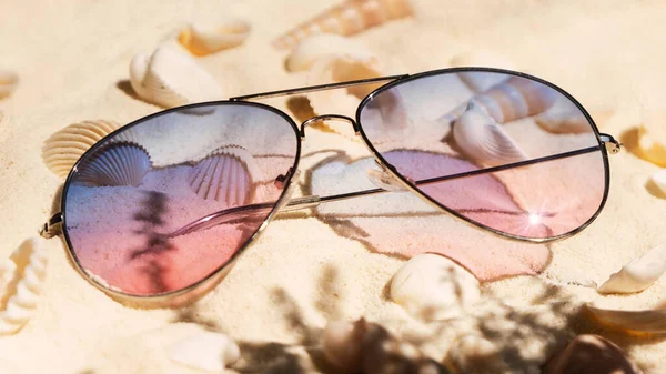海滩上的紫色和粉色渐变色太阳镜 在清澈的中性米黄色热带沙滩上有大量的贝壳 顶视图强烈的阴影背景 奢华暑假的概念 — 图库照片