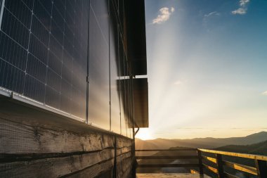 Ahşap bir kabin duvarındaki güneş panelleri. Güzel, büyük modern ev ve güneş enerjisi. Güneşin sabah ışıkları, yansımalar. Sessiz, rahatsız edici yaşam konsepti. Yenilenebilir kaynaklar. Boşluk duvar kağıdını kopyala.