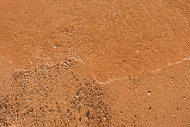 Sahildeki turuncu kum ve su dalgalarının dokusuna yakın çekim. Yaz plajı arka planı ya da seyahat duvar kağıtları, kopyalama alanı.