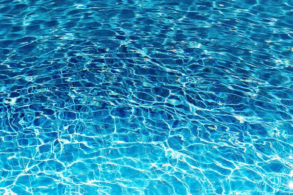 Close-up of a swimming pool filled with clear blue water. Sunlight dances on the surface, creating ripples and sparkling reflections. Summer vibes, swimming pool ads, or water backgrounds.