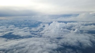 Flying among the clouds, with clouds below and above on a beautiful day. Video taken through the glass of the airplane window.