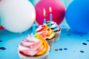 Mavi arka planda mumları olan renkli balonları olan üç kek, kutlama kartı.