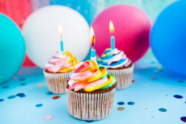 Mavi arka planda mumları olan üç gökkuşağı renkli kek renkli balonlar, kutlama kartı.