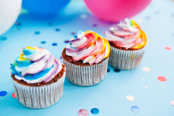 Three colorful cupcake on bright blue background with air balloons, dessert food for party
