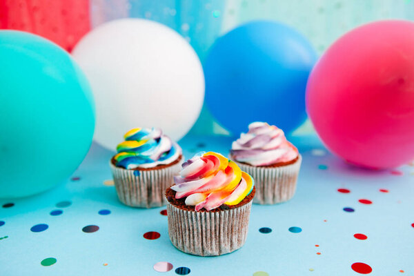 Cupcake on bright blue background with air balloons, celebration card with dessert in rainbow colors