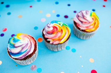 Tatlı yiyecekleri kutluyoruz - gökkuşağı renginde kek veya mavi arkaplanda simli konfetiyle kek.