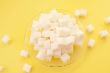 Beyaz şeker küpleri cam tabakta sarı arka planda, tatlı içerik