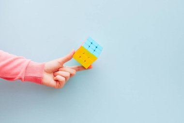 Pembe elbiseli kadın mavi arka planda Rubik küpünü, entelektüel oyunları ve beyin fırtınası konseptini gösteriyor.