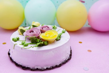 Çiçekli doğum günü pastası ve mor arkaplanlı sarı ve yeşil hava balonları.