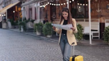 Kadın turist, arama yönü, konum haritası. Güzel, pozitif, modaya uygun gezgin bayan turist, yaz aylarında bavulla yurtdışına seyahat ederken haritada yön arıyor.