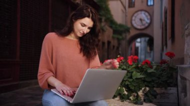 Açık havada okuyan bir öğrenci, şehir sokaklarının dekoratif taşı üzerinde çalışan bir serbest çalışan, güzel, mutlu, romantik bir kadın blogcu, online bir dizüstü bilgisayar üzerinde çalışıyor.