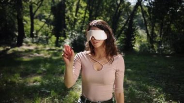 Dışarıda vr gözlüğü kullanan bir kadın, sanal gerçeklik gözlüklü güzel bir esmer kadın, doğanın bulanık arka planı ve bokeh, dışarıda vr gözlükleriyle deney yapan bir kadın.