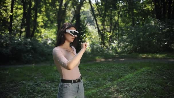 仮想現実のタッチスクリーンを使用しながら 屋外公園の芝生の上に立つ美しい女性と 将来的に自然と完全にブレンド 無限の想像力の世界です — ストック動画