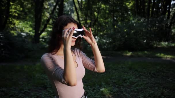 人と技術でぼやけた自然を背景に 自然を背景にVrメガネをかけながら公園でゲームをする若い女性 — ストック動画