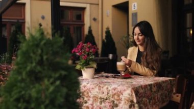 Şeker, sütlü kahve, iş kadını içkisi. Genç bir kadın yerel bir kafede kahve içiyor, gülümseyen güzel bir kız sıcak aromatik bir kapuçino içiyor, genç bir kadın