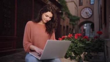 Güzel, mutlu, neşeli, güler yüzlü, romantik kadın blogcu dışarıda çalışırken online olarak çalışan, serbest çalışan, şehir sokaklarının dekoratif taşında oturan biri.