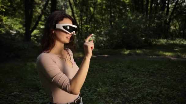 人与技术概念 自然背景模糊的室外背景 日落时分戴着Vr眼镜在公园玩游戏的年轻女性 自然背景模糊 — 图库视频影像