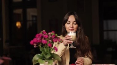 Kahve keyfi, sıcak kahve, latte içmek. Mutlu ve neşeli bir kadın bir kafede kahve içiyor, gülümsüyor, güzel ve rahatlatıcı genç bir kadın, sıcak aromatik kapuçino içiyor.