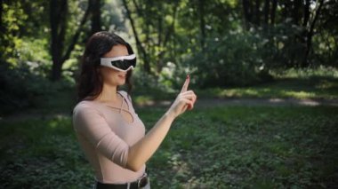 İnsanlar teknolojisi, VR gözlükleri, oyun oyunları, insanlar ve teknoloji konsepti, VR gözlüklü genç bir kadın gün batımında parkta oyun oynuyor bulanık doğa arka planına karşı.