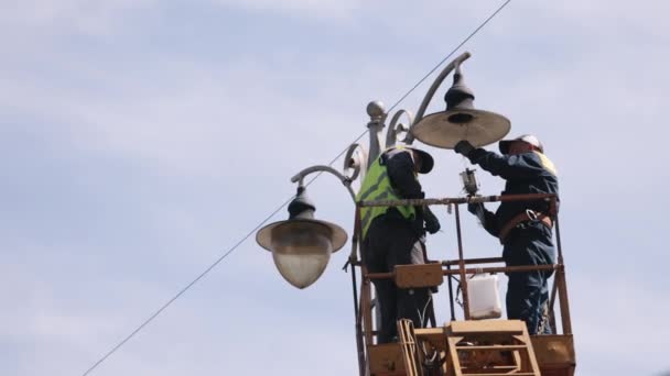 街灯を修復しバケツを持ち上げ光を固定する 労働者は街路灯の電柱灯を高さで固定し Ledライトを交換している 個人的な保護具を身に着けている人はポールランプを固定し 通りを固定する — ストック動画