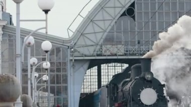 Klasik siyah buhar lokomotifi. Tarihsel tren tarlalardan geçiyor. Araç tren istasyonundan ayrılıyor. Eski buhar treni lokomotifi tren istasyonundan ayrılıyor..