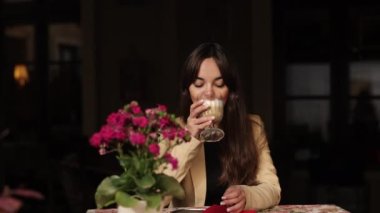 Kafeinsiz kahve, aromatik kapuçino, latte içmek. Genç ve güzel bir kadın bir kafede kahvesini yudumluyor. Neşeli bir şekilde gülümsüyor, güzel bir kız. Bir fincan sıcak kahvenin tadını çıkarıyor.