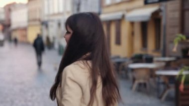 Yürüyen bir kadın, flört eden bir kadın, arka tarafı takip ediyor. Uzun saçlı bir kadın şehirde yürüyor. Dönüyor. Eğleniyor, flört ediyor, gülümsüyor.