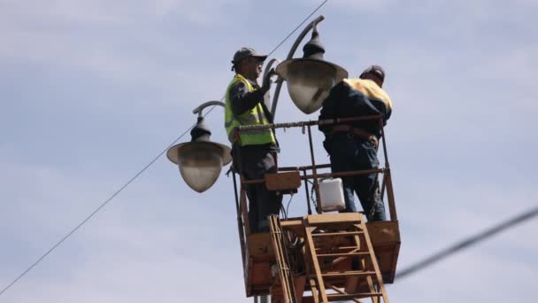 街灯ストリートライトメタルポール 街路灯の修理作業が行われ 作業者は高さで光を修復し 鉛を交換し 個人用保護具の男性リフトバケツポールランプを固定します — ストック動画