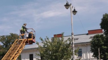 Metal direk, elektrik direği, sokak lambası. İşçiler sokak lambasını onarıyor, sokak lambalarını değiştiriyor, asansör kovasında kişisel koruma takıyor.