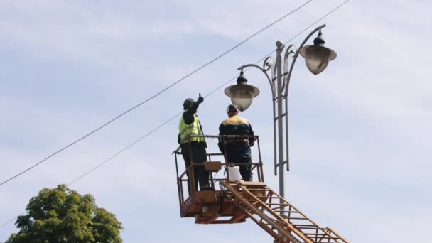 市政工作人员 设备安装 街头小灯修理工作 工人在高处修理街头小灯 安装新的铅灯 工人穿戴个人设备 — 图库视频影像