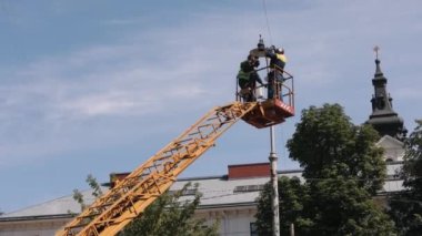 Ekipmanlar, metal direkler, sokak lambaları. Sokak lambaları için tamirat gerekiyor. İşçi, sokak lambasını tamir etmek için merdivene tırmanıyor. Erkekler ampulleri ışıkta değiştiriyor.