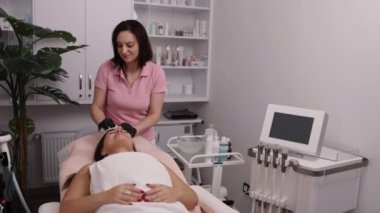 Silecek yüz, pamuk pedler, kozmetoloji kliniği. Hastanın yüzünü temizleyen güzellik uzmanı, kozmetikçi hastanın yüzünü ve boynunu pamukla siliyor.