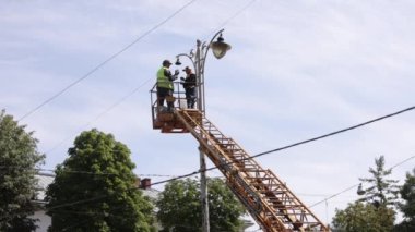 repair street lamp, crane lifted, light bulb. Worker is fixing street light pole lamp at height, replacing led lights. Men wearing personal protective equipment is fixing lamp pole lamp, fixing light