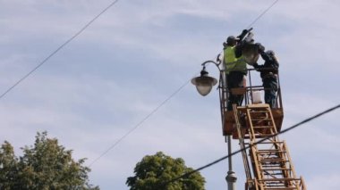replace light bulb, Municipal worker, equipment installs. Repairs are needed for street light poles. worker is climbing ladder to repair street lamp at height, changing light bulbs